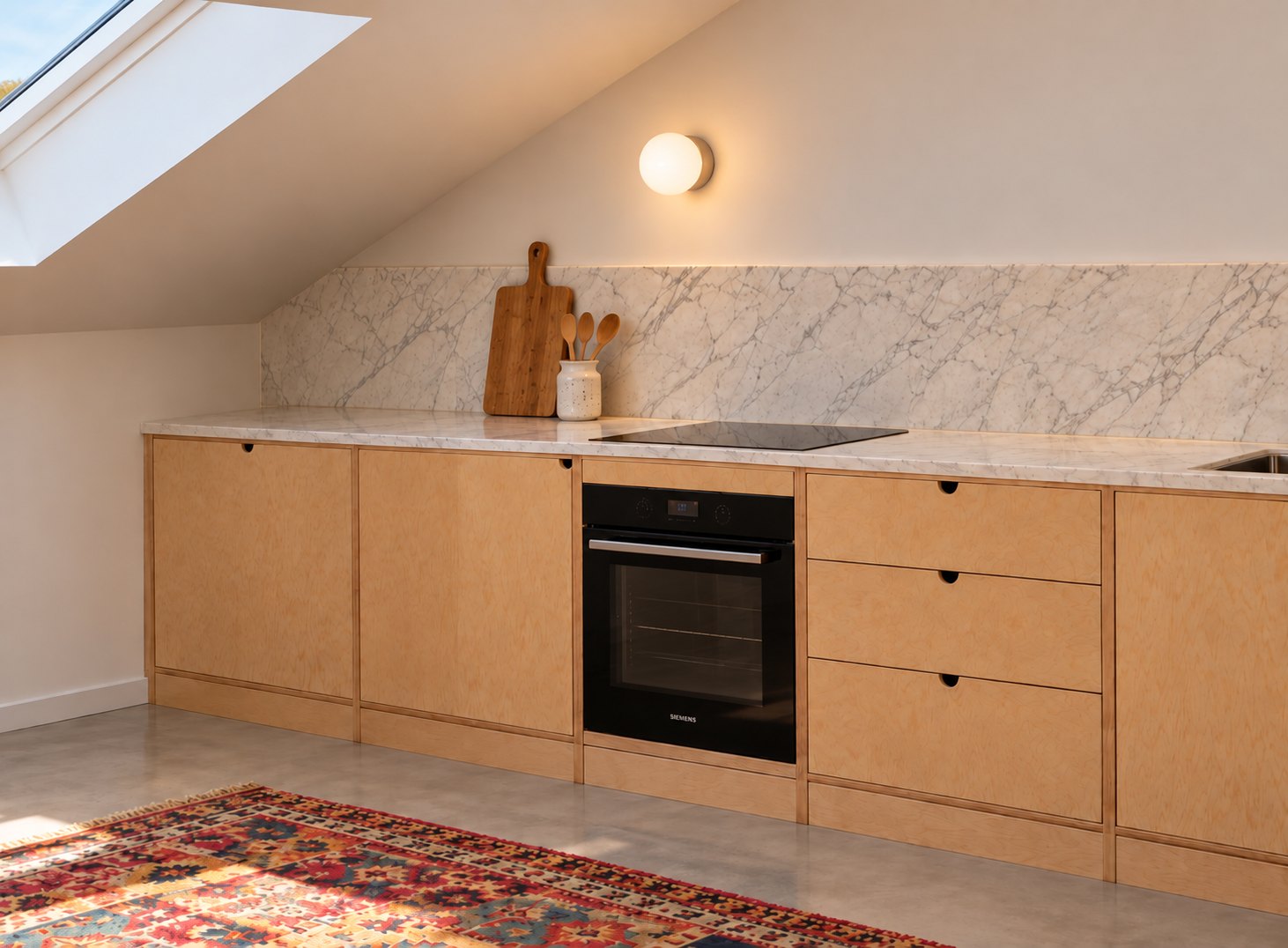 Cozinha linear de bétula sob teto inclinado, com forno integrado e bancada de mármore branco